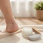 Dry, cracked heel beside a tub of moisturizing foot cream and a pumice stone for home care.